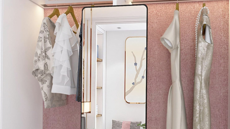 Adjustable wall-mounted mirror in a closet with hanging dresses.