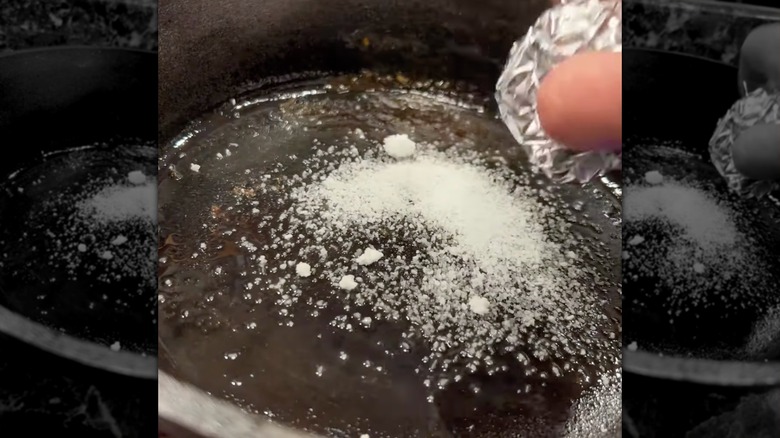 Man scrubs cast iron skillet with salt and aluminum foil to remove rust