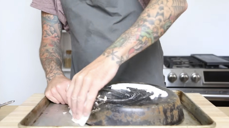 Man uses baking soda paste to scrub rust off of iron skillet