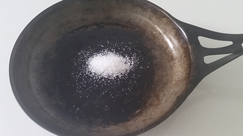 Cast iron skillet being scrubbed with salt and oil