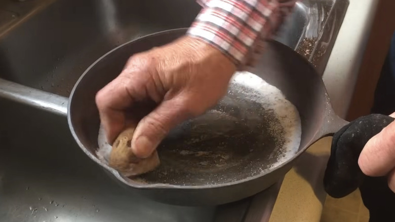 Man scrubs rust off of iron skillet with potato and salt