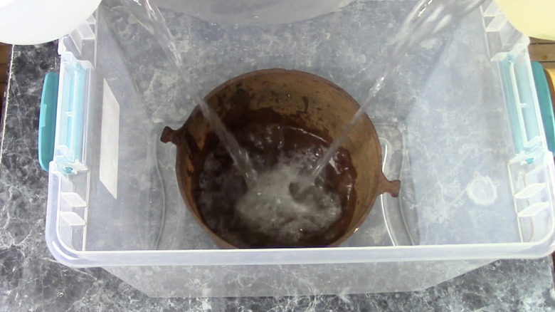 Tub with cast iron pot being soaked with vinegar and water to remove rust