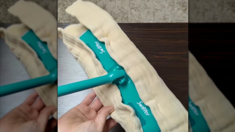 Hand holding a Swiffer mop covered by a cloth diaper