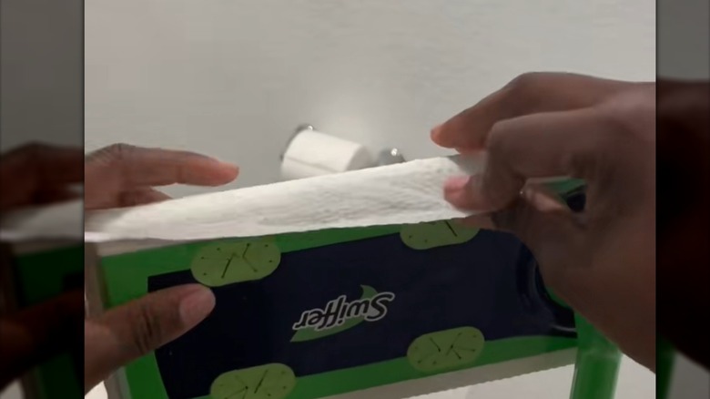 Woman puts a Clorox wipe on the head of a Swiffer mop
