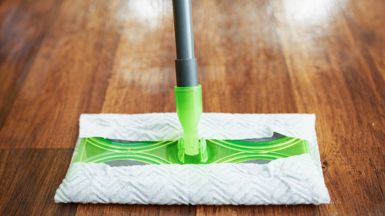 Closeup on a Swiffer green mop with cleaning cloth attached on a darker wood floor