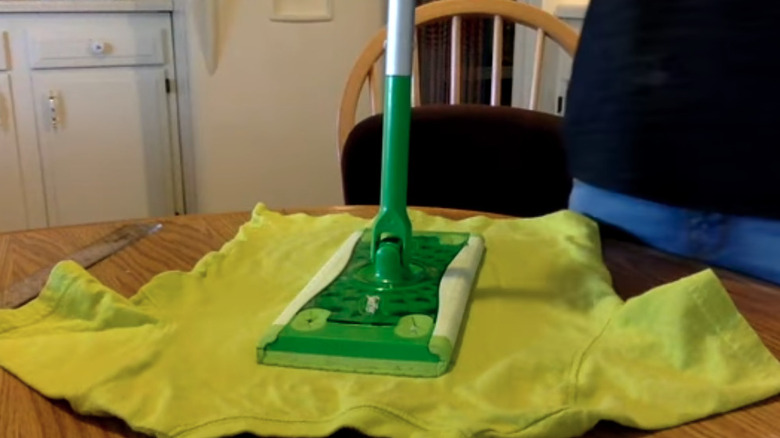 Yellow t-shirt on a table next to a ruler being used as a Swiffer mop pad
