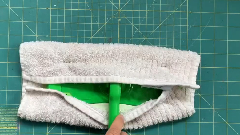Hand holding the end of a Swiffer mop with a washcloth being used as a cleaning pad on top of a cutting board