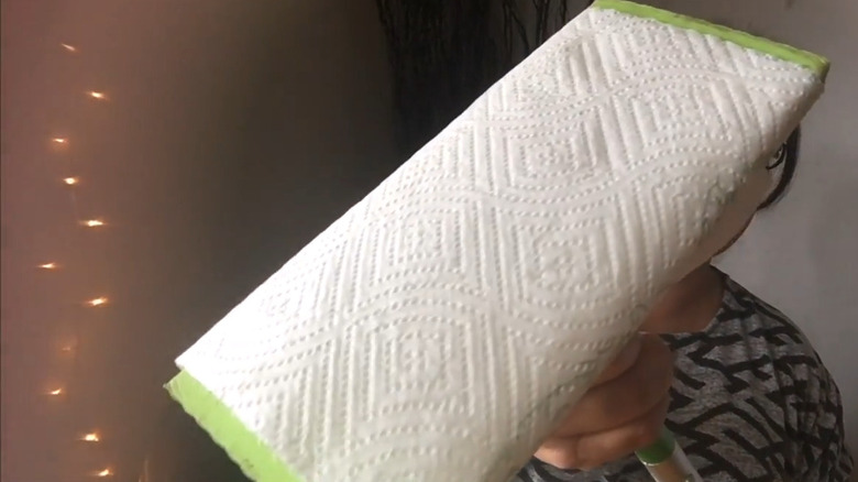 Woman with black and white patterned shirt folds paper towels over a Swiffer mop