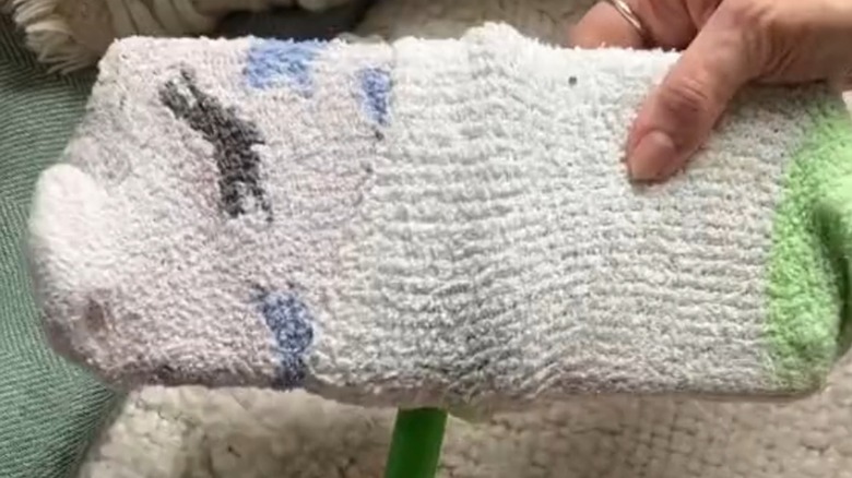 Closeup of a hand holding a Swiffer mop covered with two white socks as a pad