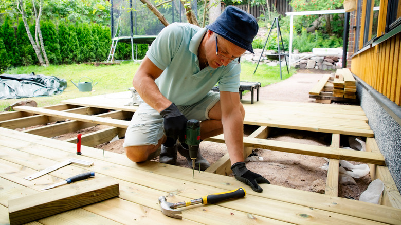 Man installing wood flooring on a deck in his yard