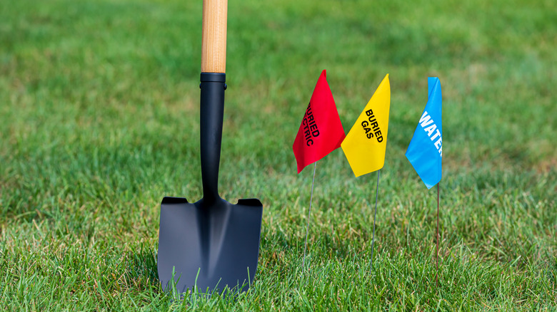 A shovel standing in the ground near a red, yellow, and blue utility flag staked into a green lawn