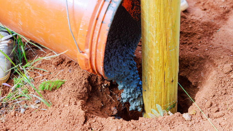 Concrete being poured into a hole with a newly installed fence post
