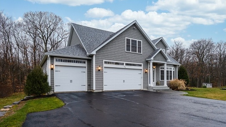 Gray house with a large wet asphalt driveway with bare trees