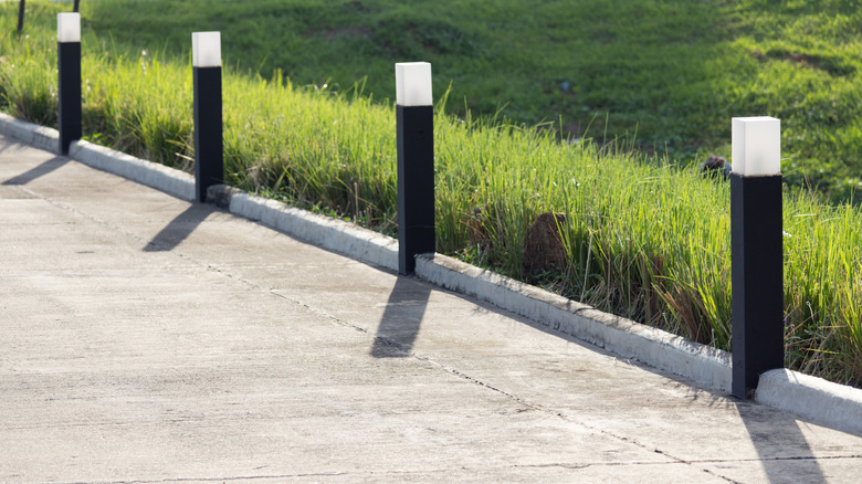 Driveway lights on square poles close together on a concrete driveway with long grass