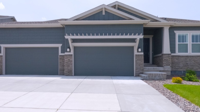 Blue house with white trim with a large white driveway with gravek edging