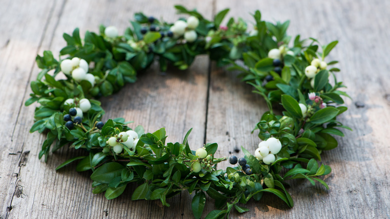 A wreath made from boxwood branches with white berries sitting on a wooden surface.
