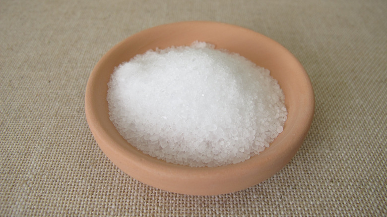 A small terra cotta-colored bowl filled with Epsom salt sits on a beige cloth surface