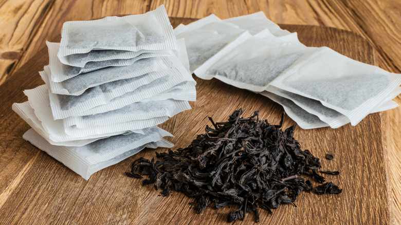 Small stacks of white tea bags, and a small pile of loose black tea, on a wooden table