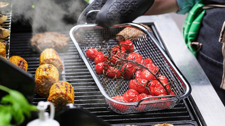A metal basket resting on a grill surface with tomatoes cooking
