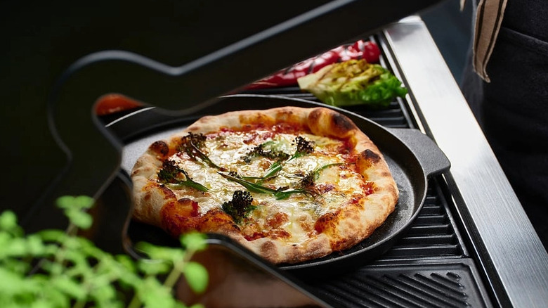 A pizza on a pizza pan being cooked on a grill