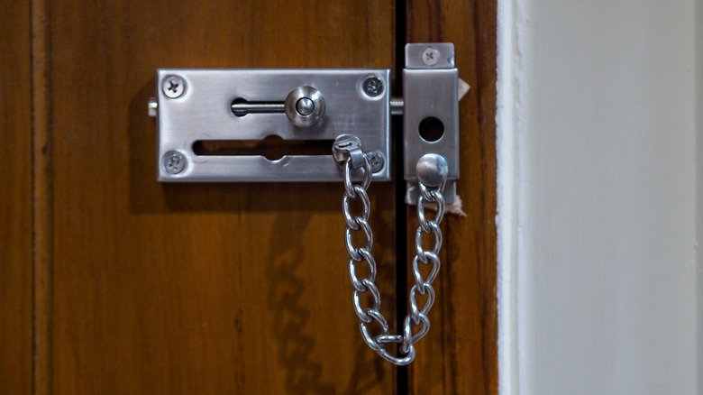 A silver metal chain lock on a wooden front door.