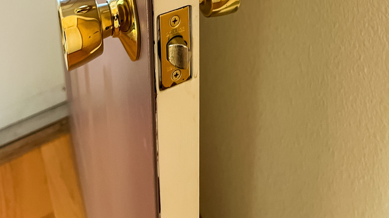 An open front door with a gold deadbolt mechanism and door handle.