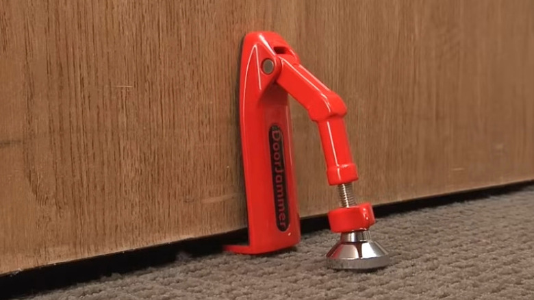 A red-painted metal door jammer inserted underneath a wooden front door.