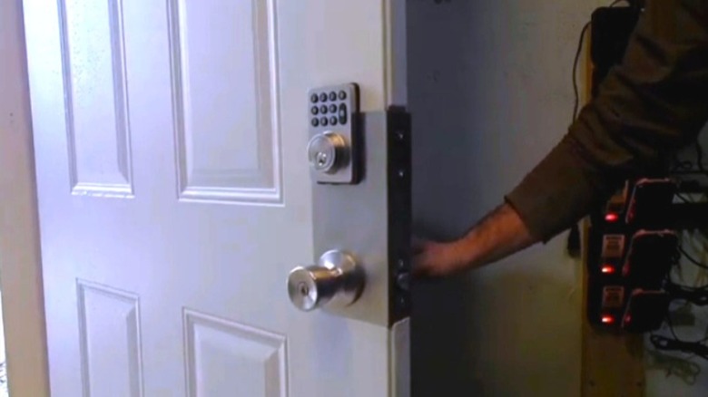 A man holds open a front door with a reinforced plate.