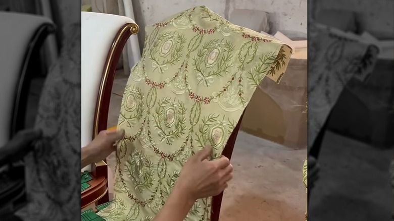 Man professionally upholsters a chair with embroidered fabric