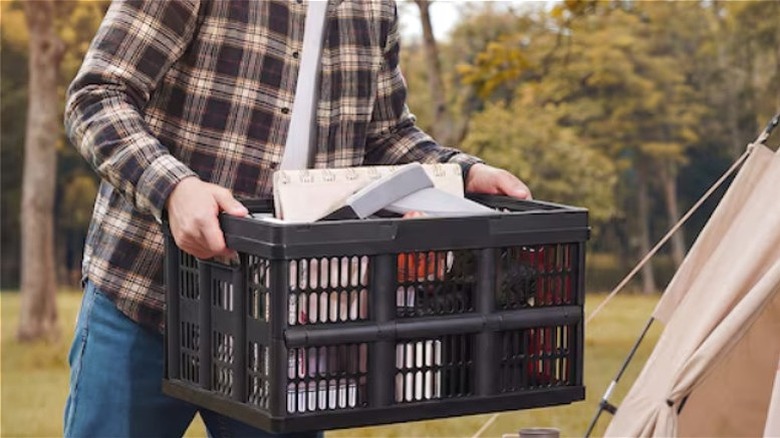 Person carrying GIVIMO collapsible storage crate with camping supplies