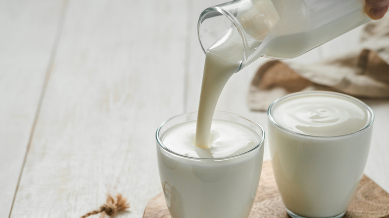 Buttermilk being poured from a glass carafe into two glasses on a wood board