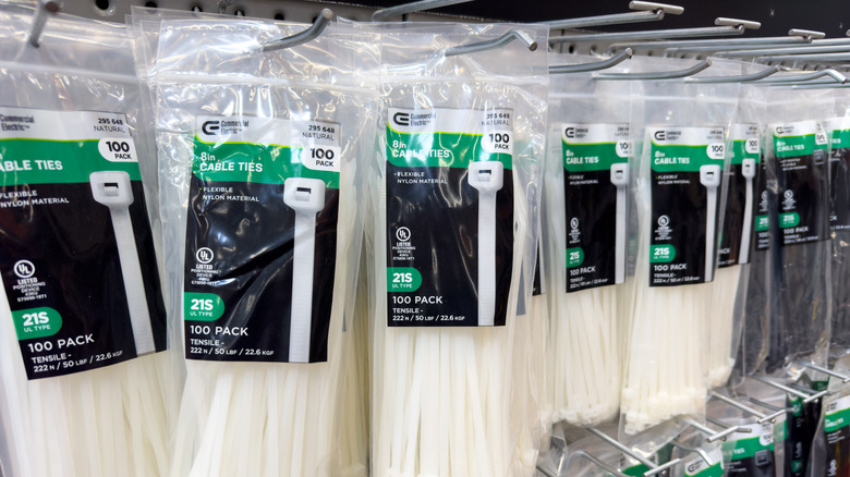 White and black cable ties in plastic packaging hanging in a display cabinet in a hardware store.