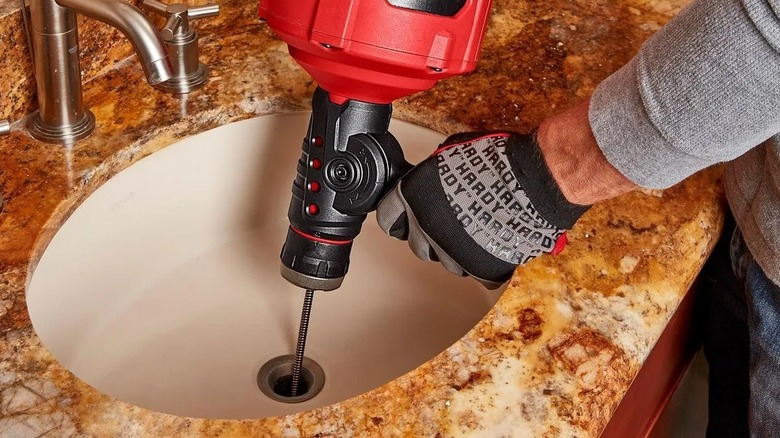 A man unclogs a sink with an electric drain cleaner.