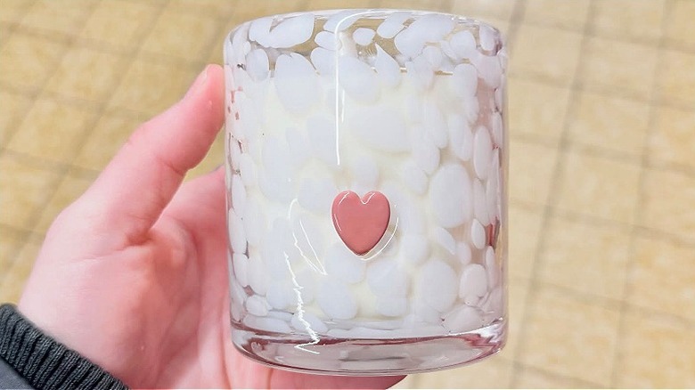 Hand holding a white glass jar candle with pink heart.