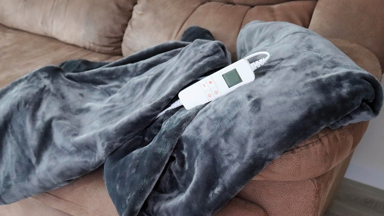 A gray heated blanket on a light brown couch, with the electronic temperature control visible