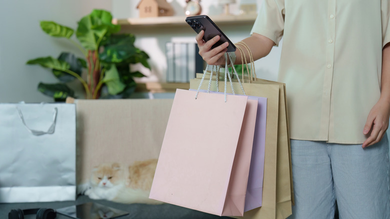 A person standing in a home holding several bags with plants and shelves in the background