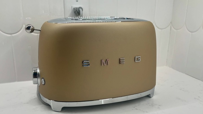 A matte metallic Smeg toaster on a white marble counter with white backsplash
