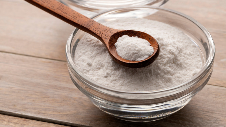 A small bowl of baking soda with a spoon on a wooden table