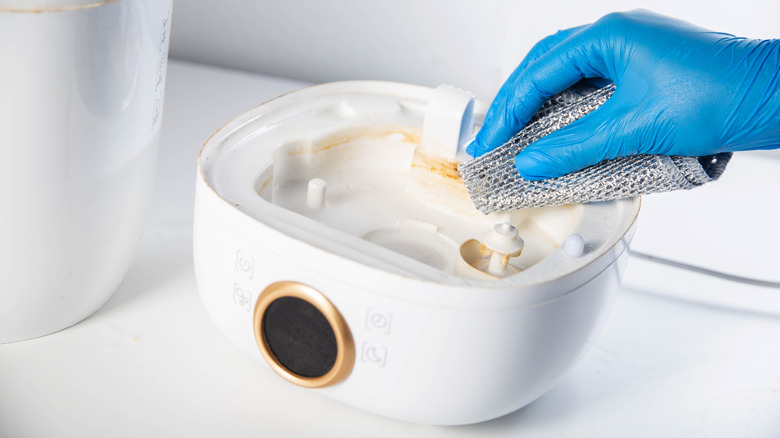 A person cleaning a humidifier while wearing gloves