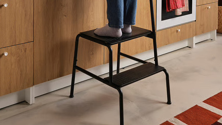 Woman standing on IKEA double step stool in front of wood cabinets