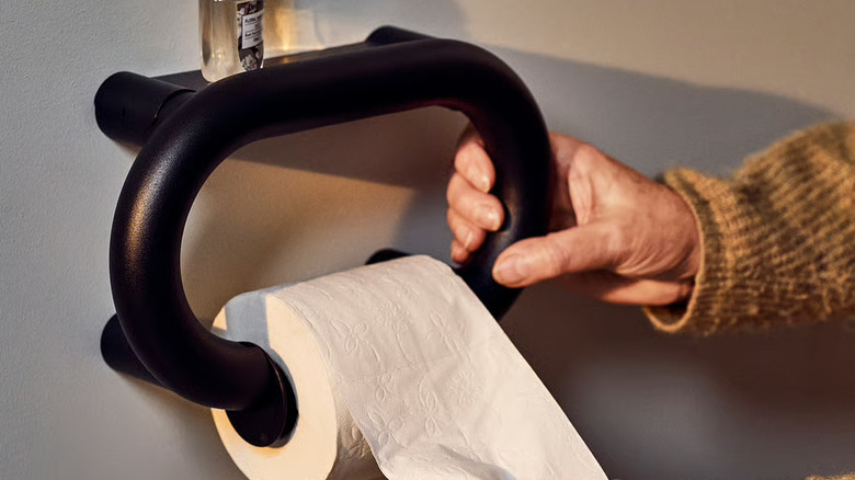 Older woman's hands reaching for toilet paper holder and handle