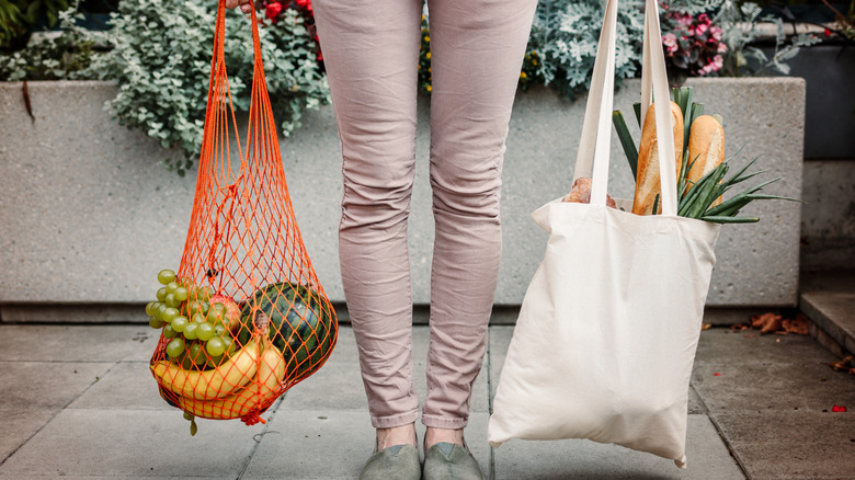 Woman holding two reusable shopping bags with groceries in them