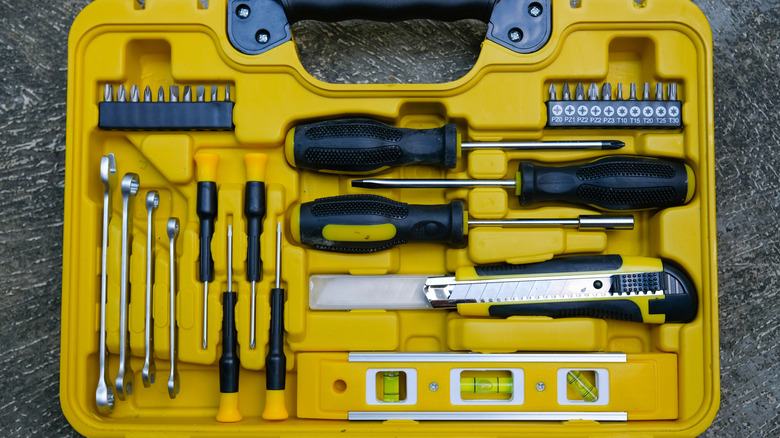 A yellow tool box with a variety of tools and accessories laid out in designated spots