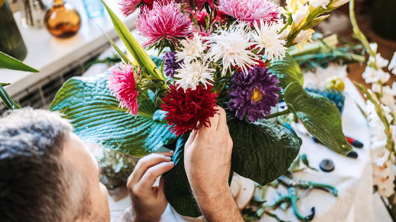 A light skinned man arranges cut flowers in a vase.