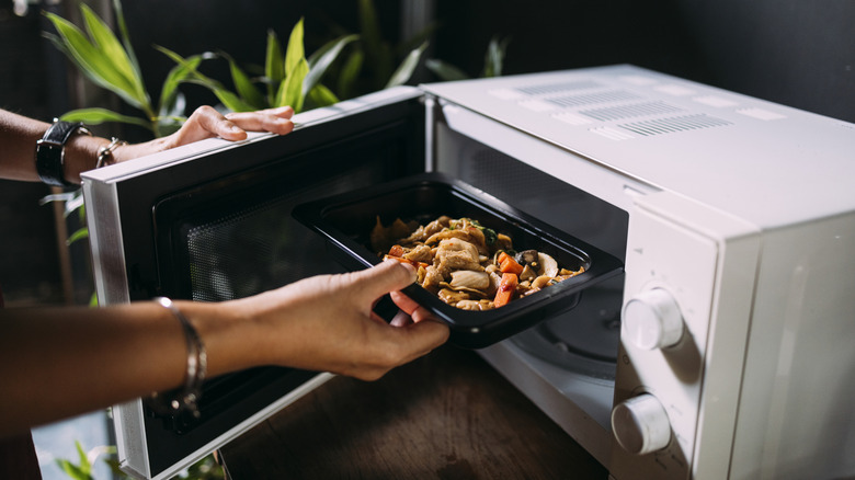 A woman placing a plate of food in a white microwave.