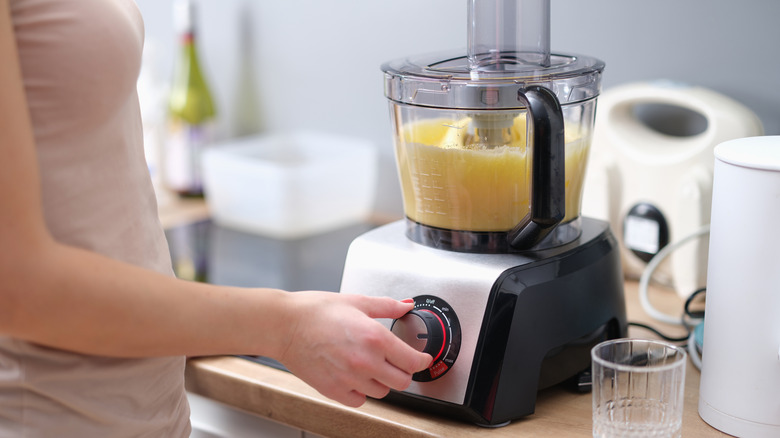 A woman operating a food processor on a kitchen counter.