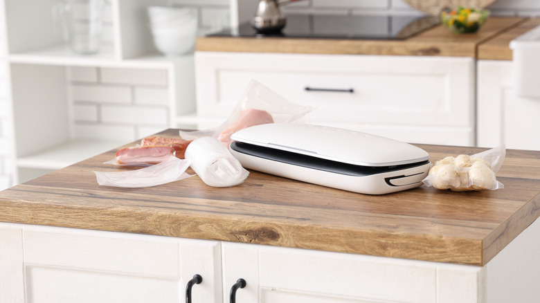 A white vacuum cleaner on a wooden counter with sealed bags of mushrooms and meat beside it.