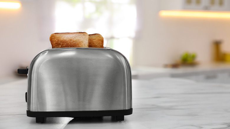 A stainless steel toaster on a marble counter with two slices of bread in it.