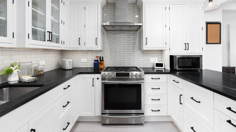 A kitchen detail with white cabinets, subway tile backsplash, stainless steel appliances, and black quartz countertops and hardware.