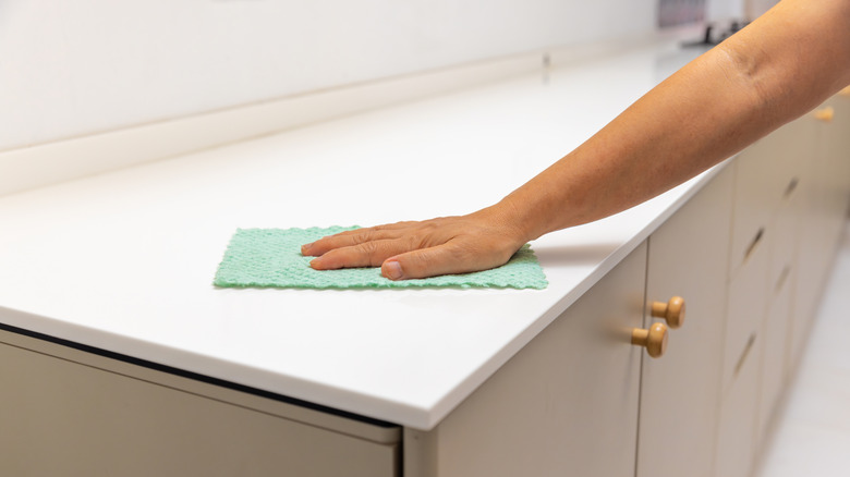 person wiping down solid white countertop with rag